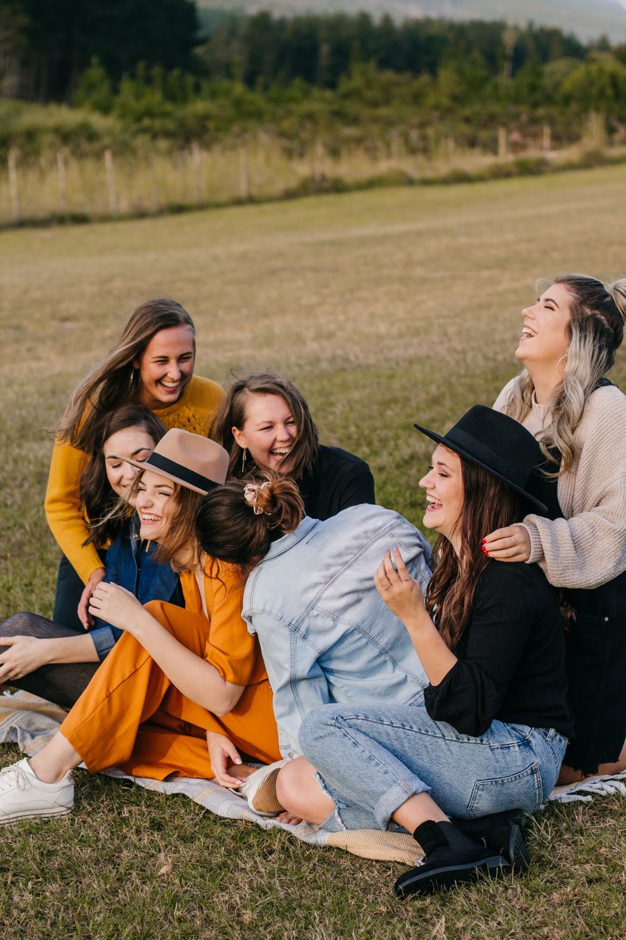A group of friends in mustard and denim laughing together on a grassy field